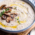 Creamy mushroom soup topped with sautéed mushrooms, fresh herbs, and a drizzle of olive oil